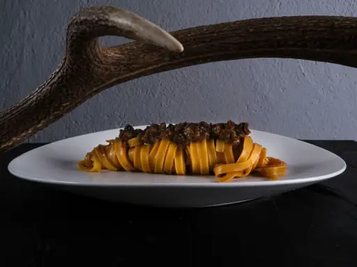 Un piatto di pasta fresca con ragù di cinghiale, un'autentica esperienza di mangiare toscano, con un palco di cervo sullo sfondo.
