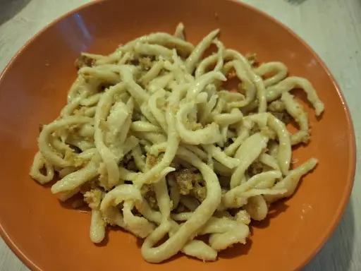 Pici fatti in casa con un saporito sugo per i pici, serviti in un piatto arancione.