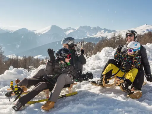 Famiglia felice in slittino sulla montagna per bambini in estate, con neve e montagne innevate sullo sfondo.