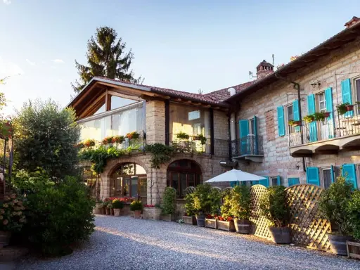 Un incantevole agriturismo in Piemonte, con un cortile acciottolato, balconi fioriti e persiane azzurre.