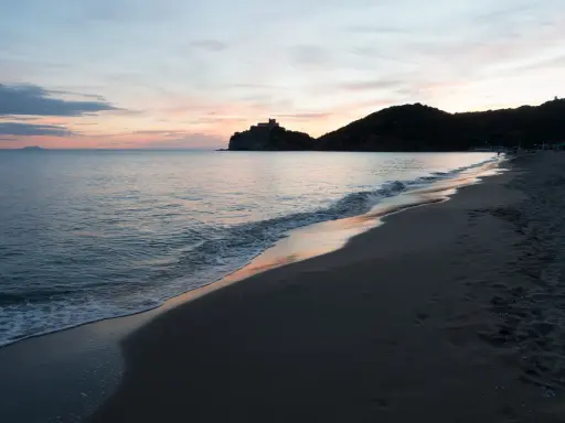 Tramonto sulla costa della Toscana, con un castello su una collina e il mare calmo. Un ricordo di vacanza con un neonato.