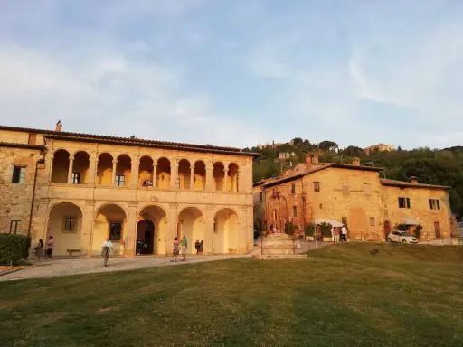 Edificio storico con portico ad archi, un pozzo e persone che passeggiano. Un luogo che sembra uscito da uno dei tanti film girati a Montepulciano.