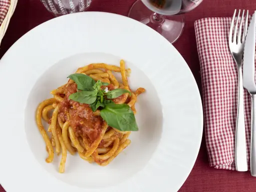 Pici al sugo, un classico della ricetta aglione Val di Chiana, serviti su un piatto bianco con basilico fresco.
