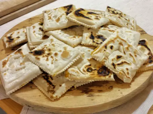 Piatto tipico cesenate: piadina fritta, dorata e leggermente bruciacchiata, servita su un tagliere di legno.
