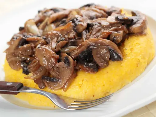 Polenta con funghi trifolati, un classico tra i cibi tipici del Trentino Alto Adige, pronta per essere gustata.