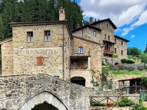 Antico ponte in pietra e case in pietra, tipici dei borghi vicino Arezzo, immersi nel verde della campagna toscana.