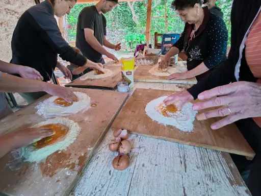 Bambini e adulti impastano farina e uova in una fattoria in Abruzzo, un'esperienza culinaria all'aperto.