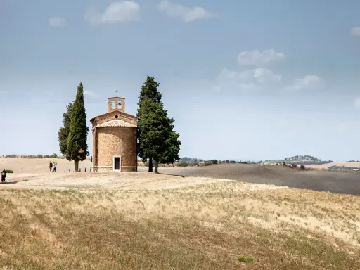 Cappella della Madonna di Vitaleta, icona della Val d'Orcia, circondata da cipressi e dolci colline toscane sotto un cielo azzurro.