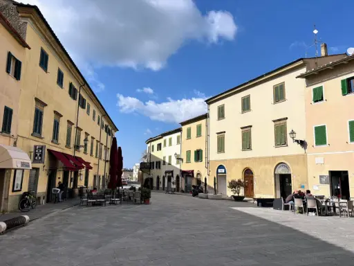 Piazza soleggiata a Pomarance, con edifici storici, tavolini all'aperto e scorci suggestivi da scoprire.