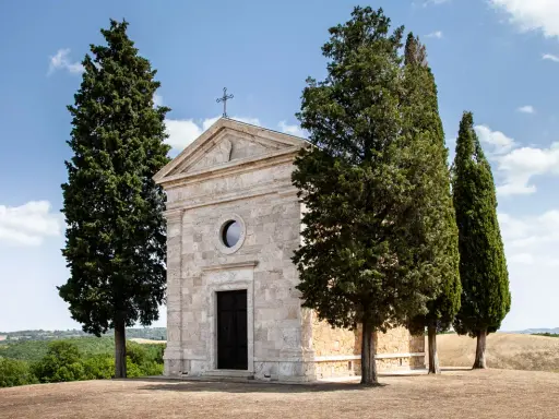 La chiesa di Vitaleta, con i suoi cipressi iconici, si erge solitaria su una collina toscana sotto un cielo azzurro.