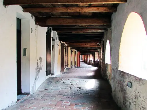 Portico con soffitto in legno e archi luminosi, pavimentazione in mattoni antichi. Un viaggio nella storia lungo la via degli asini a Brisighella.