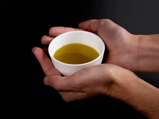 Mani che sorreggono una tazzina bianca con olio evo. Il suo significato è prezioso, un nettare dorato.