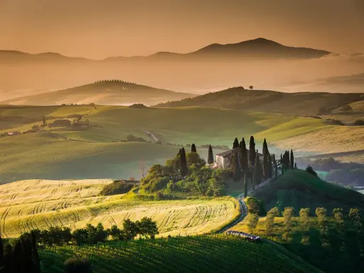 Dolci colline verdi e un casale con cipressi nel Val d'Orcia. Ideale da visitare in primavera o autunno per colori e luce perfetti.