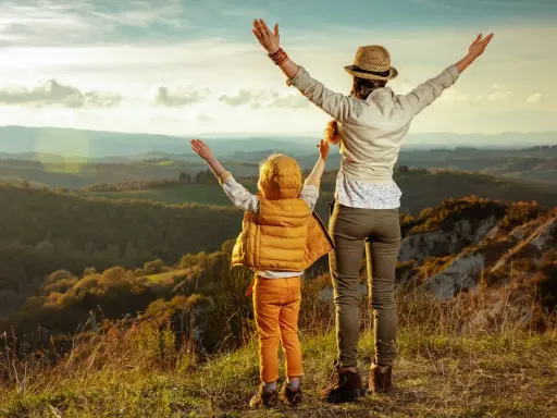 Bambini in Toscana, con le braccia al cielo, ammirano un paesaggio collinare al tramonto.