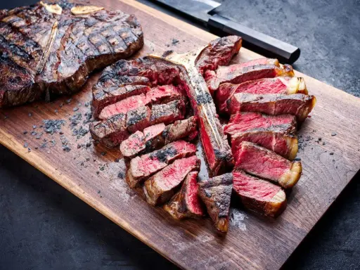Una succulenta fiorentina alla griglia, affettata e servita su un tagliere di legno, con sale grosso sparso.