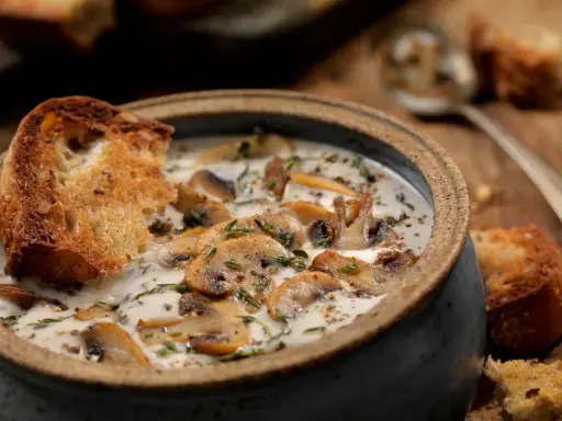 Una cremosa zuppa di funghi toscana, arricchita da erbe aromatiche e servita con crostini di pane abbrustolito.
