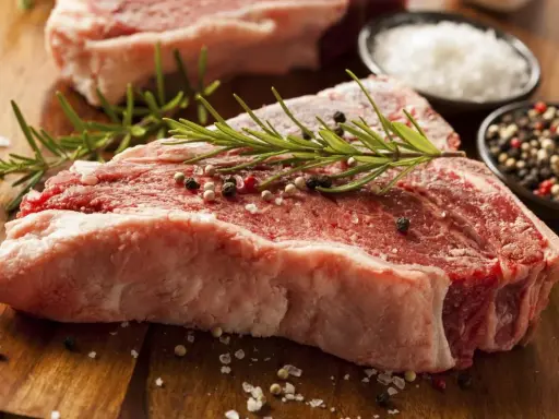 Bistecca alla fiorentina, un cibo succulento pronto per essere cucinato, con rosmarino, sale grosso e pepe.