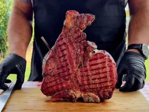 Un cuoco con guanti neri mostra una succulenta bistecca alla fiorentina appena grigliata, pronta per essere servita. Un esempio perfetto di come cucinare la bistecca alla fiorentina.