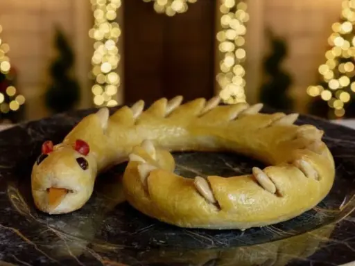 Dolci tipici Perugia: un serpente di pasta frolla dorata, con occhi rossi e lingua arancione, adagiato su un piatto scuro.