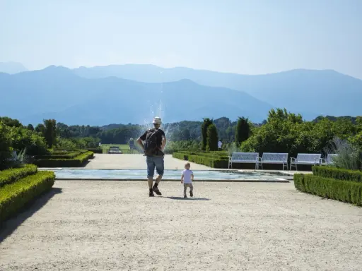 Un uomo e un bambino passeggiano in un giardino curato, con fontane e montagne sullo sfondo. Una giornata perfetta in Piemonte con bambini.