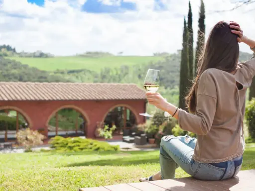 Donna con bicchiere di vino, vista su un casale con archi, paesaggio collinare. Un'oasi di pace tra gli agriturismi particolari Lombardia.