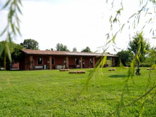 Un'accogliente fattoria didattica alle Fornaci, con un edificio rosso, balle di fieno e un prato verde.