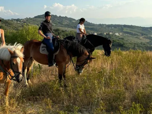 Tre ragazze in sella a cavalli godono di splendide passeggiate a cavallo in Abruzzo, tra colline verdi e cielo azzurro.