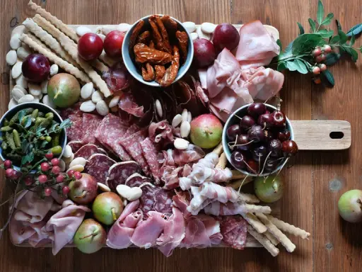 Tagliere con salumi tipici lombardi, frutta, sottaceti e grissini su un tavolo di legno.