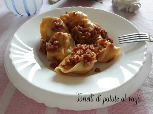 Tortelli di patate al ragù, un piatto gustoso e confortante, servito su un piatto bianco con una forchetta.