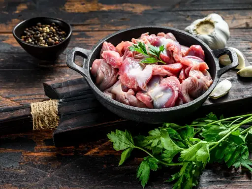 Piatto toscano con interiora di pollo crude in padella, con aglio, pepe e prezzemolo su tagliere di legno scuro.