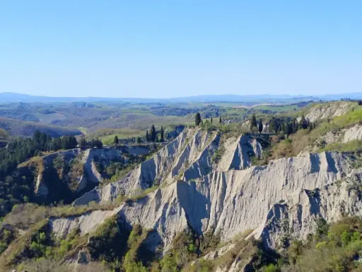Paesaggio lunare con calanchi toscana, creste erose e vegetazione verdeggiante sotto un cielo azzurro.