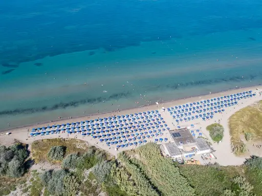 Spiaggia attrezzata con ombrelloni blu, ideale per campeggi in Toscana sul mare per bambini. Acqua cristallina e gente che si gode il sole.