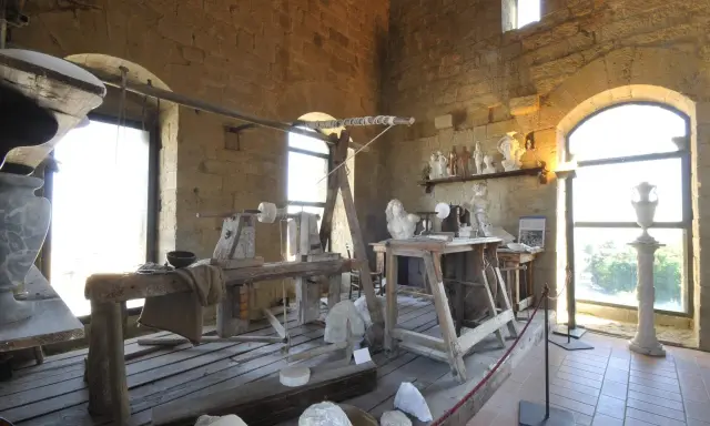 Laboratorio di scultura con attrezzi antichi e statue in marmo, che evoca la tradizione dell'alabastro toscana.