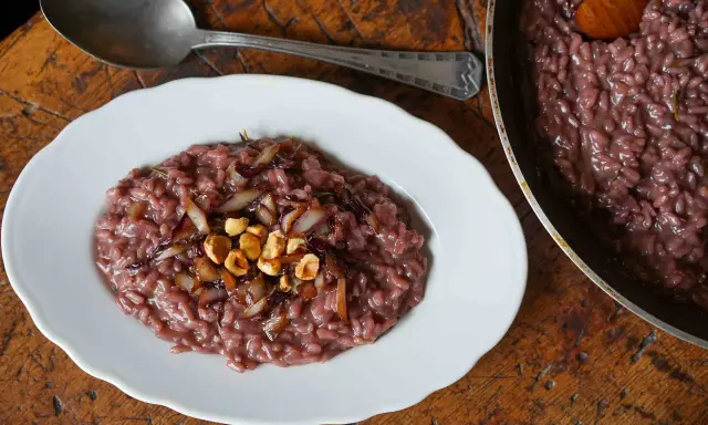 Risotto rosso con cipolla caramellata e nocciole, un classico tra i piatti tipici di Verona, servito su un piatto bianco con un cucchiaio d'argento.