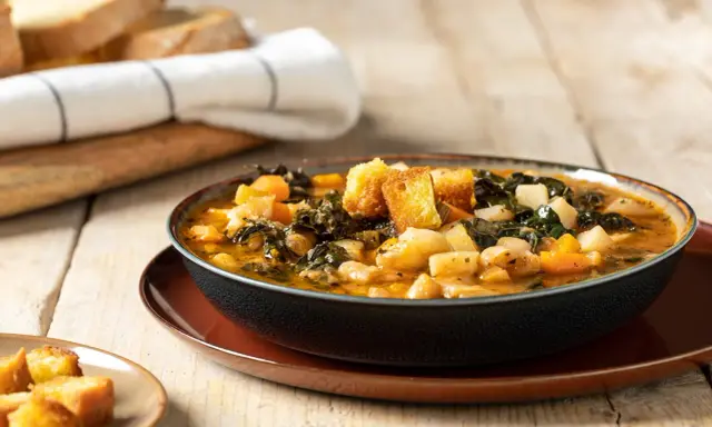 Una ciotola fumante di zuppa di cavolo nero e fagioli cannellini, guarnita con crostini dorati, su un tavolo di legno rustico.