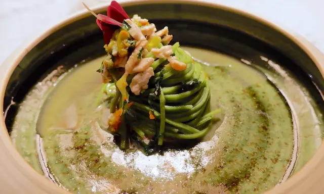 Un nido di spaghetti verdi con verdure e carne, guarnito con un fiore rosso. Un assaggio dei piatti tipici Avellino.