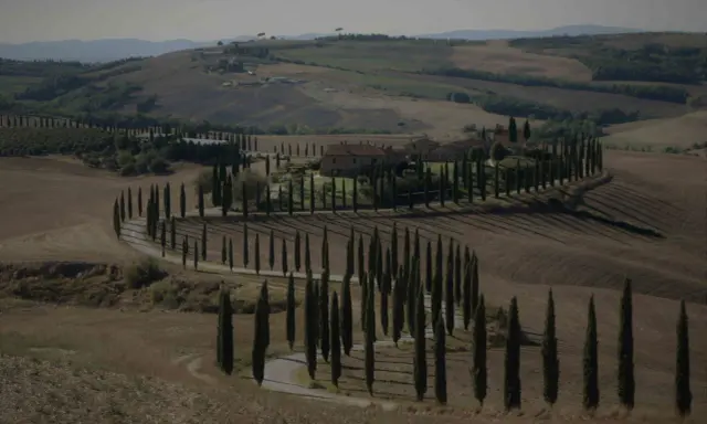 Un casale nel Val d'Orcia autunno, circondato da cipressi che disegnano curve sinuose su dolci colline.