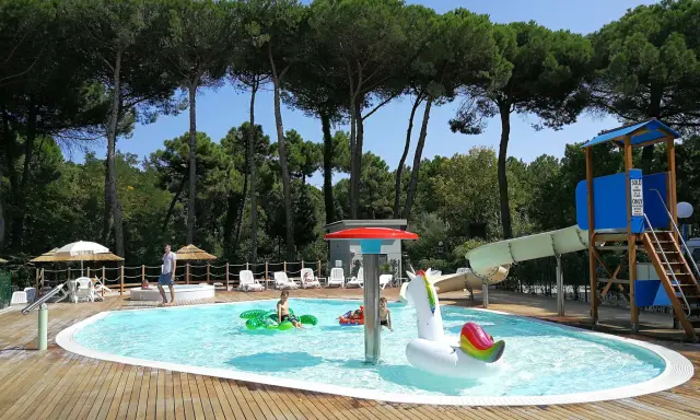 Bambini felici in piscina con gonfiabili, scivoli e giochi d'acqua. Perfetti campeggi Emilia Romagna per bambini, un'oasi di divertimento sotto i pini.