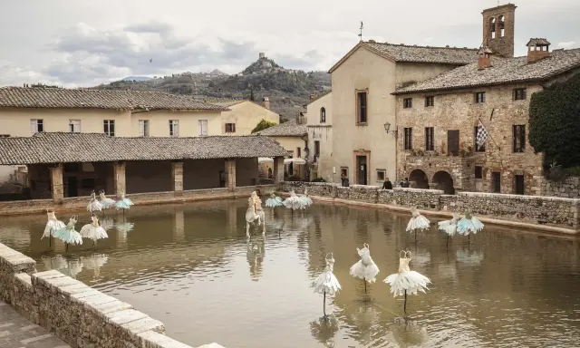 Bagno Vignoni: cosa vedere? La vasca termale con installazioni artistiche di abiti da ballo e un cavallo bianco.