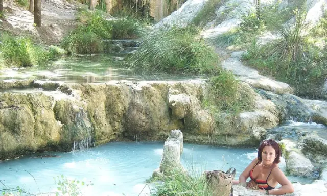 Donna rilassata nelle acque termali di Borgo San Filippo, tra rocce calcaree e vegetazione lussureggiante.