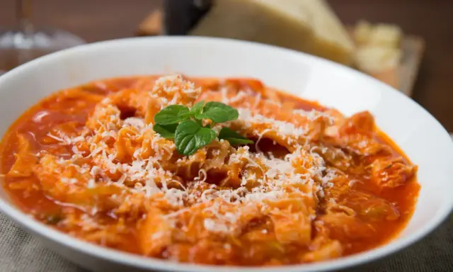Trippa alla romana, uno dei piatti tipici del Lazio, servita in una ciotola bianca con parmigiano grattugiato e una fogliolina di menta.
