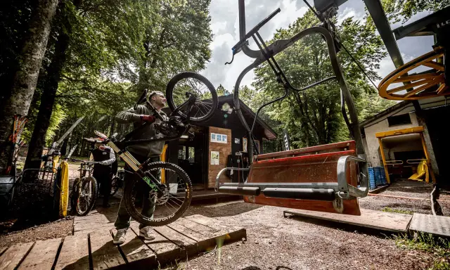 Ciclista porta la sua bici verso gli impianti di risalita ad Amiata, pronto per un'avventura in mountain bike.