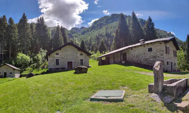 Agriturismi lombardia montagna: casette in pietra immerse nel verde, con boschi e montagne sullo sfondo.