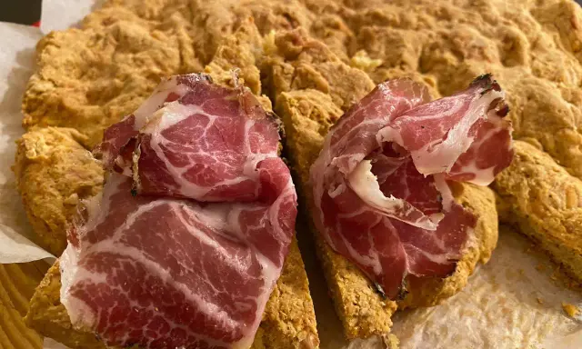 La ciaccia di Pasqua toscana, fragrante e dorata, è guarnita con fette di salume rosa.
