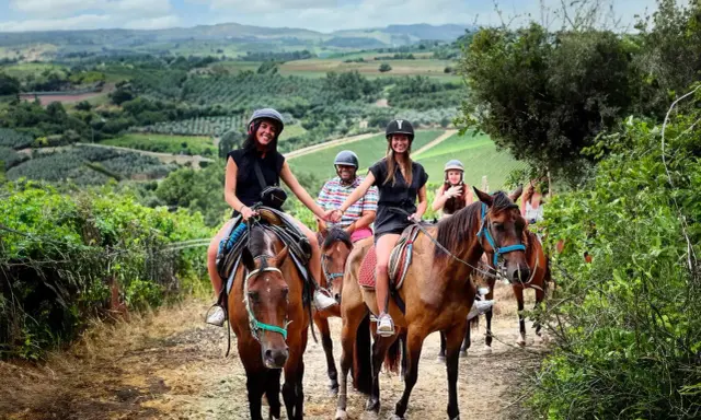 Un gruppo di amici si gode una **passeggiata a cavallo toscana** tra colline verdi e vigneti. Sorridono felici, immersi nella bellezza del paesaggio.
