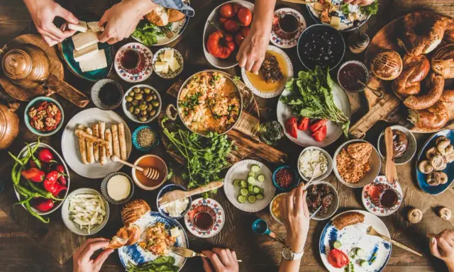 Un ricco banchetto per vacanze enogastronomiche: formaggio, olive, pane, miele, verdure fresche e piatti caldi, tutto condiviso in un'atmosfera conviviale.