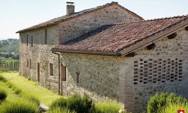 Un casale in pietra e mattoni, ideale per vacanze in Umbria montagna, immerso nel verde con tetto in coppi e un muro traforato.