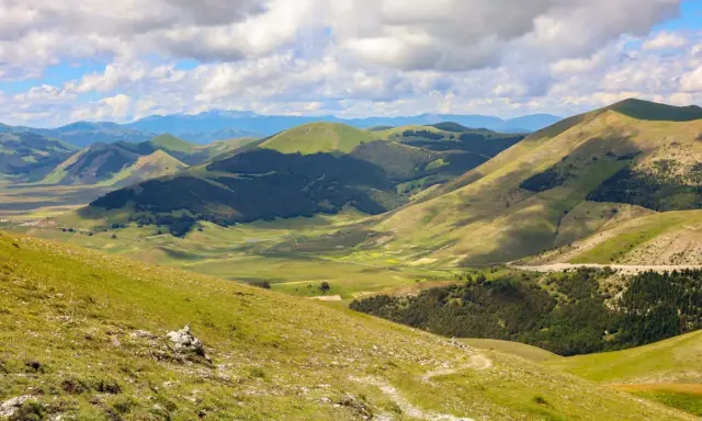 Panoramica dei Monti Sibillini, un paesaggio verdeggiante con dolci colline e valli, ideale per scoprire cosa vedere in questa zona.