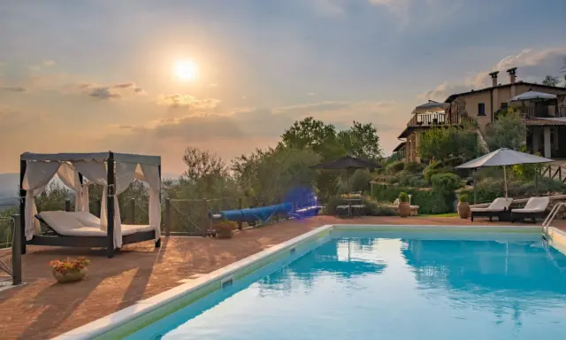 Piscina con lettini e gazebo, ideale per sapere dove dormire in Toscana. Tramonto suggestivo su un casale.