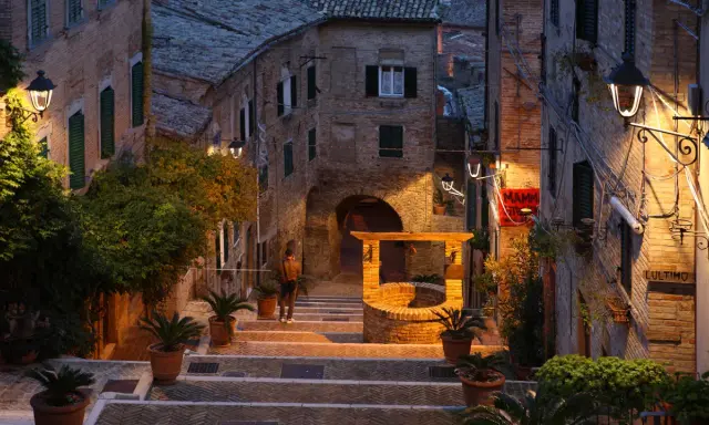 Un vicolo suggestivo a Montefeltro, cosa vedere: un pozzo antico, scalinate in pietra e luci soffuse creano un'atmosfera magica.